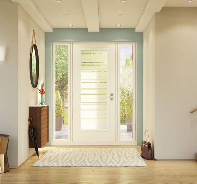 A modern, well-lit entryway features a white door with glass sidelites, a wooden side table with a red flower vase, and a round mirror on the wall. A striped rug lies on the light wood floor, with a brown bag placed next to the stairway.